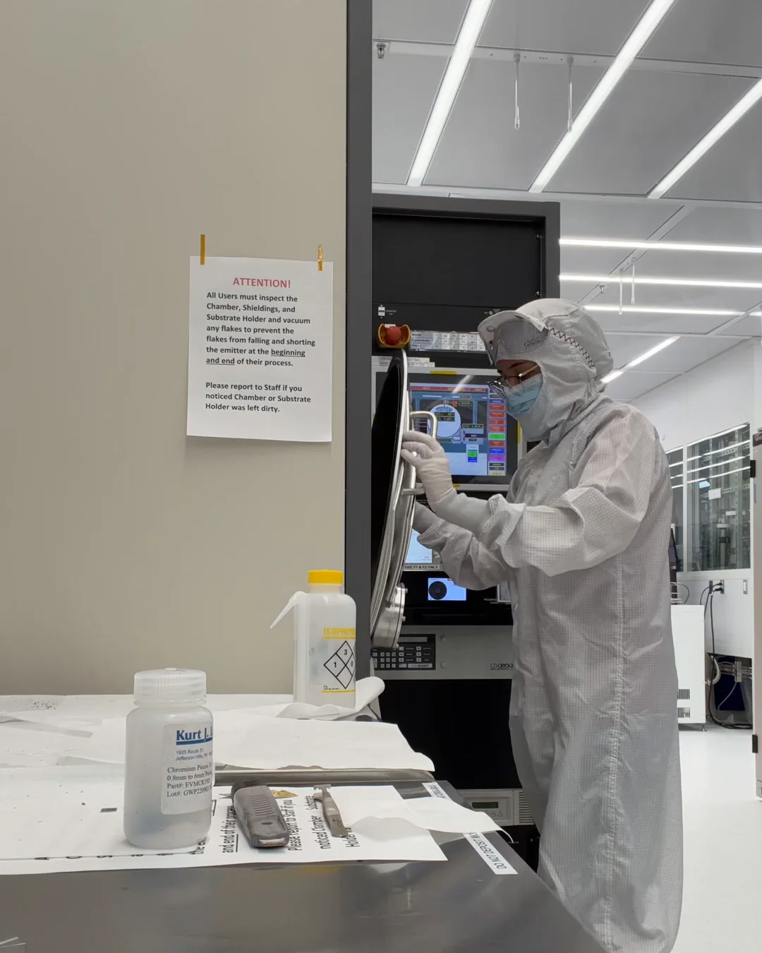 Victoria in a full cleanroom gown, hood, mask and gloves, opening the chamber door of a deposition tool