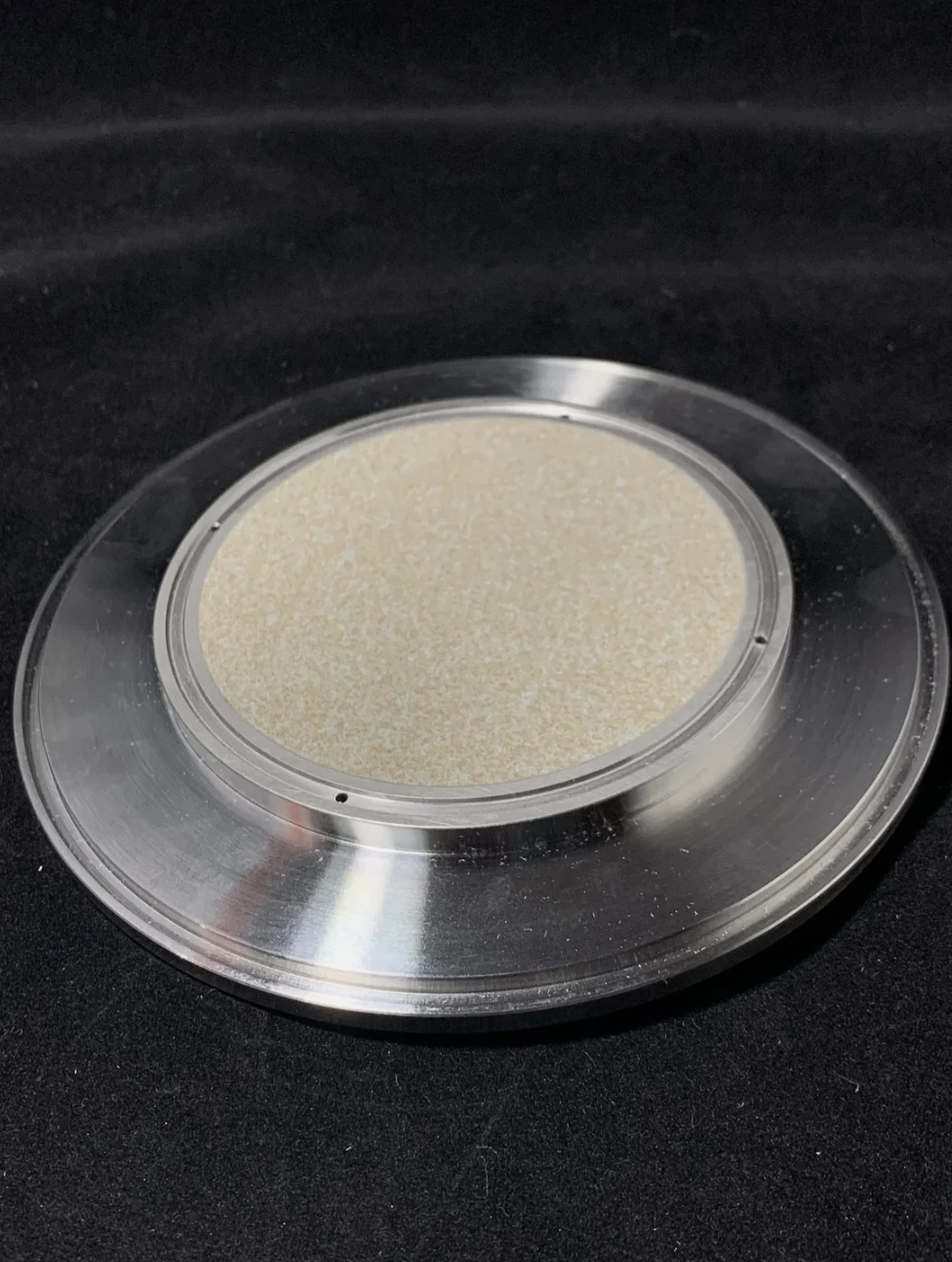 Round vacuum chuck: a porous ceramic face set in a machined metal body with a stepped flange and small holes around the ceramic
